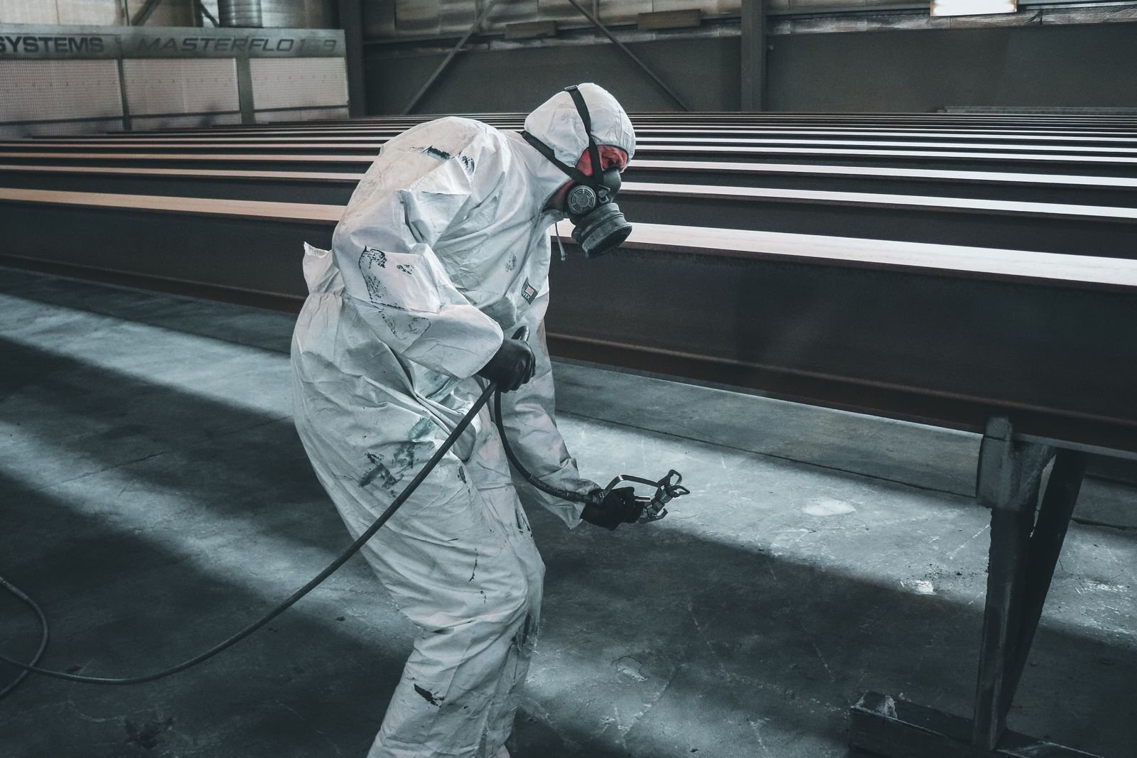 Worker in protective suit spray-coating steel beams